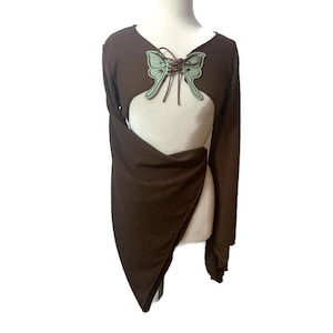 May include: A brown long-sleeved top with a unique design. The top features a cutout in the front and a draped, asymmetrical hem. A decorative butterfly is attached at the neckline. The butterfly is light green with brown lacing.