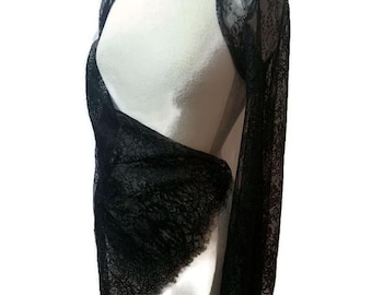 May include: A black lace bolero with long sleeves and an open front design. The garment features a delicate floral pattern throughout the sheer fabric, with scalloped edges along the hem and cuffs, draped over a white mannequin torso.
