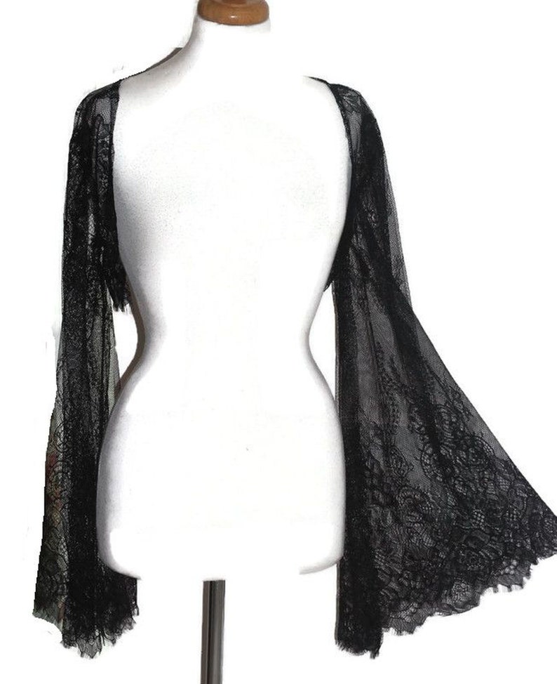 May include: Black lace shrug with long, flowing sleeves. The shrug is sheer and delicate, with a floral pattern.