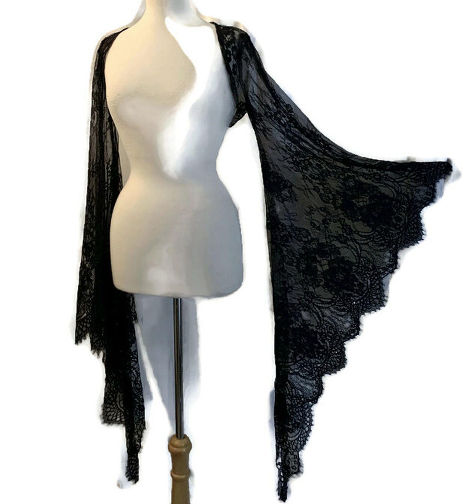 Black lace triangle shawl with a gothic floral pattern, displayed on a dress form with dramatic scalloped edges and draped sleeves.