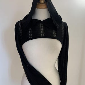 May include: A black long-sleeved bolero shrug featuring an attached hood and a collar. The garment is crafted from a sheer, lightweight fabric with a subtle vertical striped pattern throughout the sleeves and the main body of the piece.