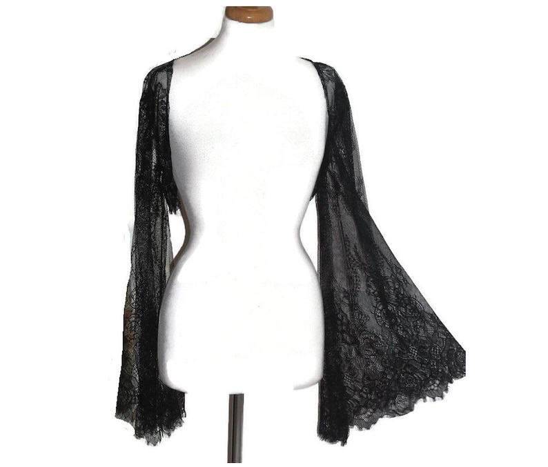 May include: Black lace shrug with long bell sleeves. The shrug is sheer and delicate, with a floral pattern.