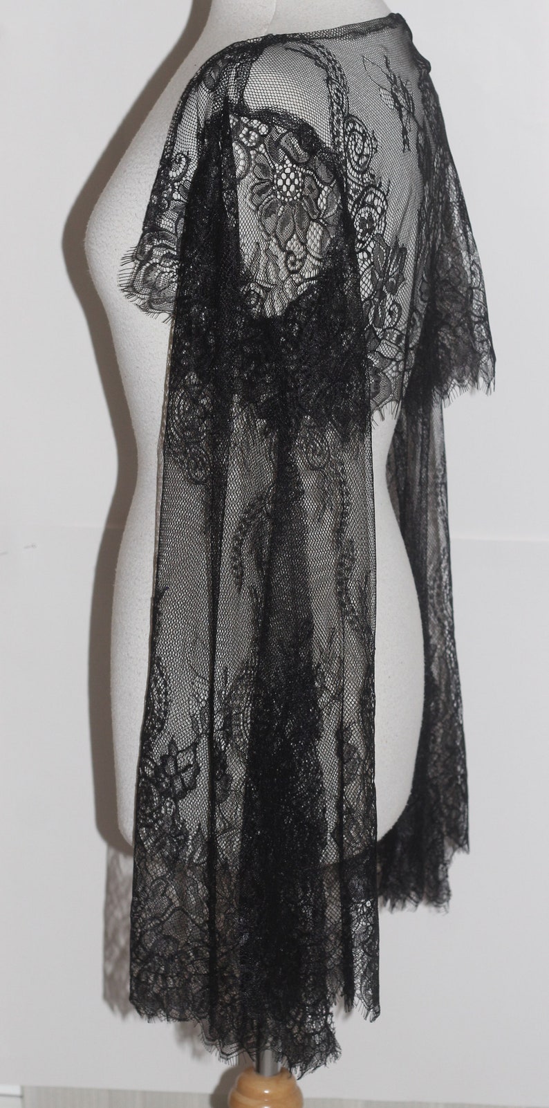 May include: Black lace shawl with a delicate floral pattern. The shawl is sheer and has a flowing design.
