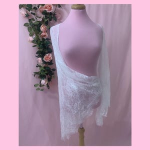 Front view of a white eyelash lace bridal shrug featuring extra wide, dramatic flared bell sleeves over a wedding gown.