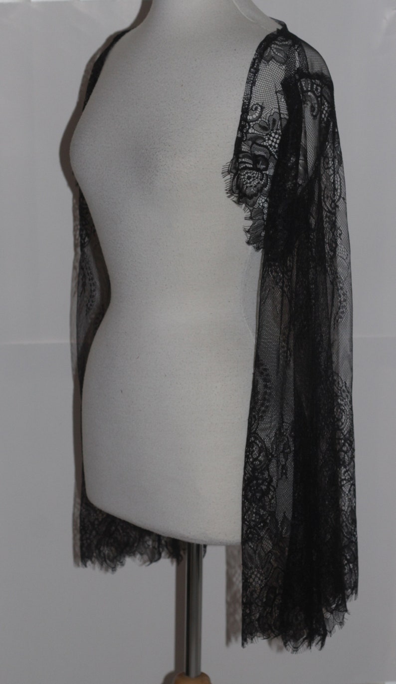 May include: A black lace shawl with a delicate floral pattern. The shawl is sheer and lightweight, and it would be perfect for adding a touch of elegance to any outfit.