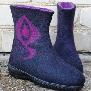 May include: A pair of dark purple felt boots with a pink design on the front. The boots have a black rubber sole.