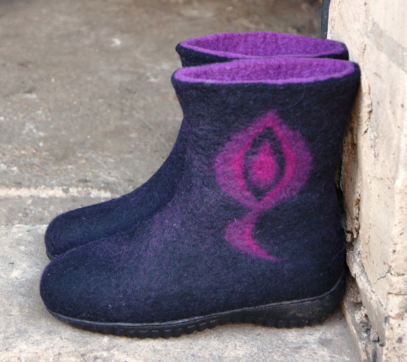 May include: A pair of black felt boots with a pink and purple design. The boots have a rounded toe and a thick sole.
