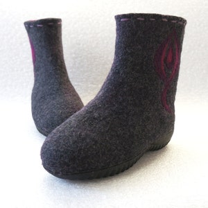 May include: A pair of gray felt boots with a pink and red design on the front. The boots have a black rubber sole.
