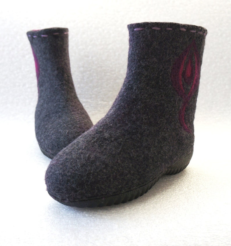 May include: A pair of gray felt boots with a pink and red design on the front. The boots have a black rubber sole.