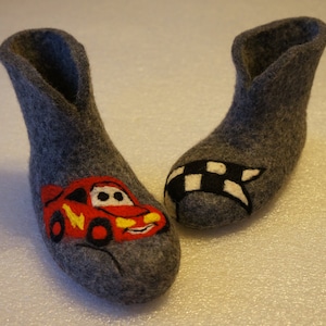 Puede incluir: Un par de zapatillas de fieltro gris con un diseño de coche rojo y una bandera a cuadros. Las zapatillas son suaves y acogedoras, perfectas para mantener los pies calientes en invierno.