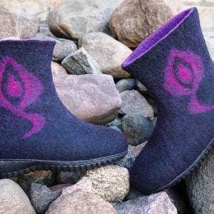 May include: A pair of black felt boots with a purple and pink design. The boots have a rubber sole and are sitting on a pile of rocks.