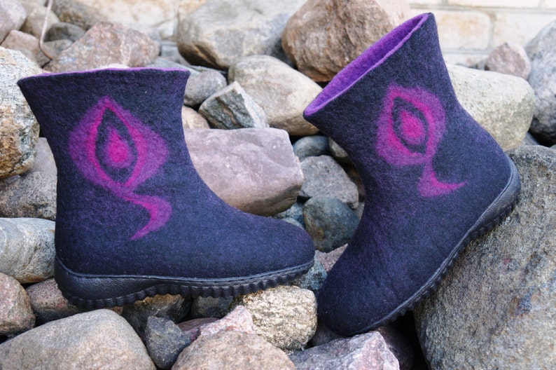 May include: A pair of black felt boots with a purple and pink design. The boots have a rubber sole and are sitting on a pile of rocks.