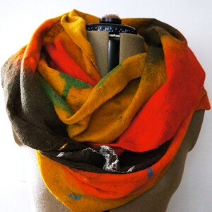 Puede incluir: Una bufanda de lana colorida con tonos de naranja, amarillo, verde y marrón. La bufanda está doblada y drapeada sobre un maniquí.