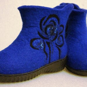 Puede incluir: Un par de botas de fieltro azul con diseños florales negros. Las botas tienen una suela de goma negra.