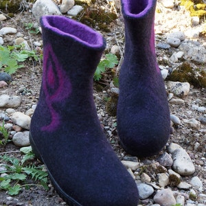 May include: A pair of black felt boots with purple accents. The boots have a rounded toe and a short heel. The boots are sitting on a bed of rocks and moss.