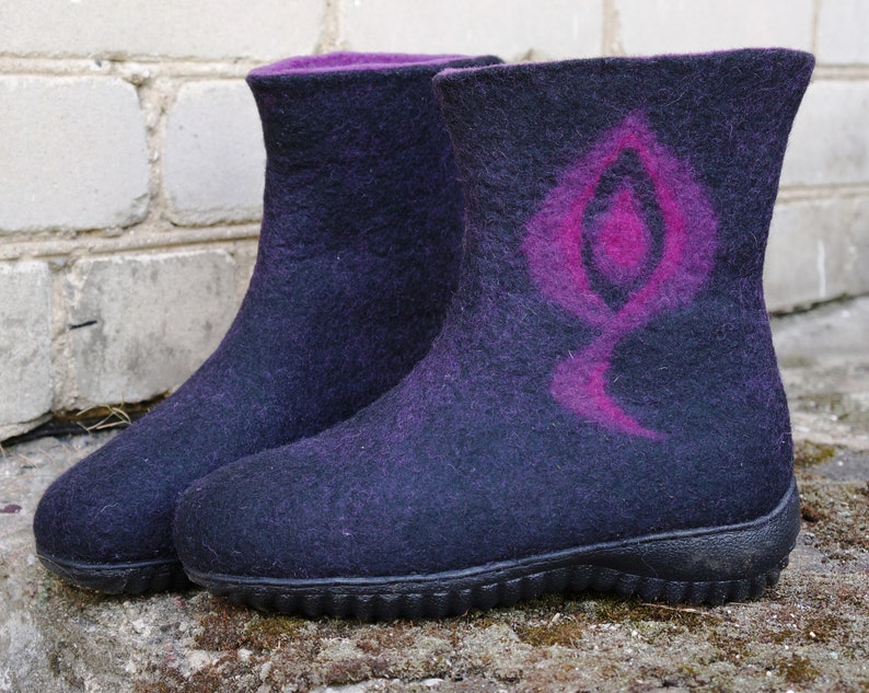 May include: A pair of black felt boots with a pink design on one boot. The boots have a rubber sole.