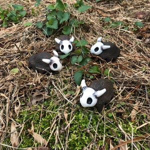 May include: Four small, brown ceramic animal figurines with white painted faces and horns. The figurines are arranged on a bed of dry grass and moss.
