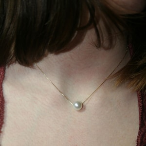 A single round white pearl on a thin gold chain, worn on a woman.