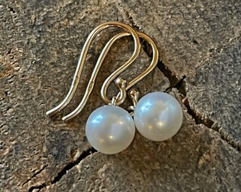 May include: A pair of gold pearl earrings with a simple hook design. The pearls are white and round.