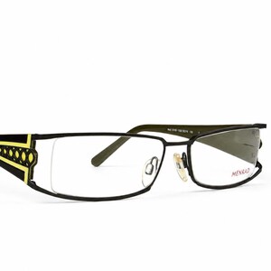 May include: Black spectacles with rectangular lenses and a yellow geometric cutout pattern on the temples. The frame features a thin metal bridge, adjustable nose pads, and the brand name MENRAD printed in red on the right lens surface.