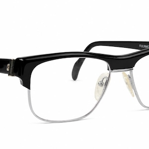 Könnte beinhalten: Schwarz-silberne Browline-Brille mit glänzend schwarzem Oberrahmen und dünnen silbernen Metallrändern unten. Das rechte Brillenglas zeigt den Markennamen Louis Feraud und ein kreisförmiges Logo in schwarzer Schrift. Die Bügel sind schwarz.