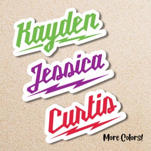 May include: Three name stickers in green, purple, and red, each with a white border and a lightning bolt design. The names are "Kayden", "Jessica", and "Curtis". The text "More Colors!" is in the bottom right corner.