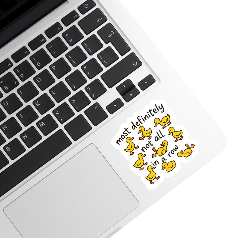May include: A white sticker with the text "most definitely not all in a row" and cartoon yellow ducks. The sticker is on a laptop.