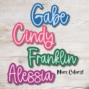 May include: Four colorful, handwritten names: Gabe, Cindy, Franklin, and Alessia. The names are cut out of vinyl and have a white outline. The text "More Colors!" is in black at the bottom of the image.