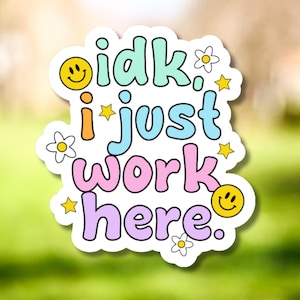 May include: A colorful sticker with the phrase "idk. i just work here." in bubble letters. The sticker features a smiley face, stars, and flowers in shades of yellow, orange, blue, pink, and purple.