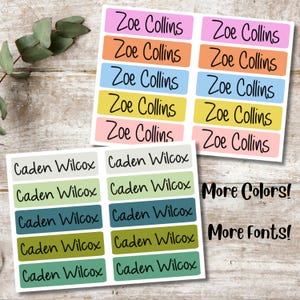 May include: A set of colorful personalized name labels with the names "Zoe Collins" and "Caden Wilcox" printed on them. The labels are rectangular and have a variety of colors, including pink, orange, blue, yellow, and green. The text "More Colors!" and "More Fonts!" is also included on the labels.