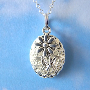May include: Silver necklace with a round locket pendant featuring a delicate flower design. The locket has a filigree pattern and is openable.