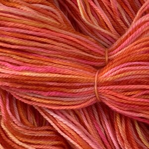 May include: Close-up of a skein of yarn in shades of orange, pink, and red. The yarn is soft and fluffy, and the colors are vibrant and rich.
