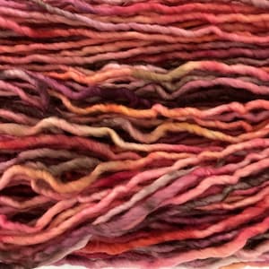 May include: A close-up of a skein of yarn in shades of pink, red, and orange. The yarn is soft and fluffy, and it is perfect for knitting or crocheting.