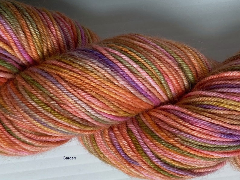 May include: A skein of multicolored yarn with shades of pink, orange, green, and purple. The yarn is called "Garden".