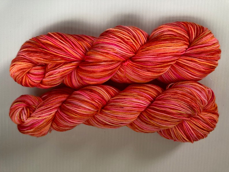 May include: A skein of yarn in a multi-colored stripe pattern of red, orange, pink, and white.