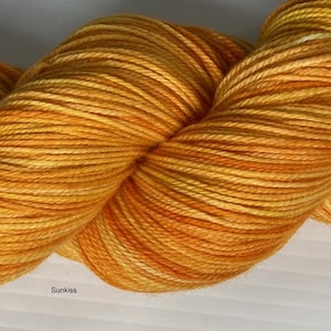 May include: A skein of yarn in a bright orange and yellow colorway with a subtle white variegation. The yarn is called "Sunkiss".