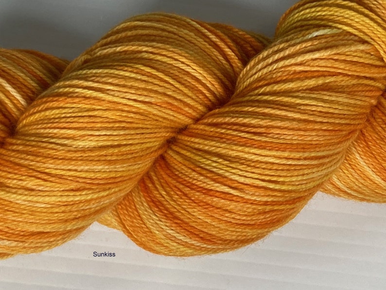 May include: A skein of yarn in a bright orange and yellow colorway with a subtle white variegation. The yarn is called "Sunkiss".