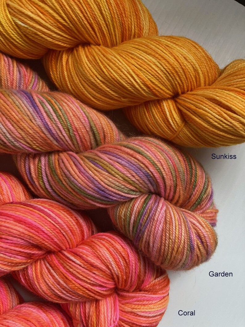 May include: Three skeins of yarn in shades of orange, pink, and purple. The yarn is labeled "Sunkiss", "Garden", and "Coral".