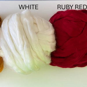 May include: Four bundles of fiber in gold, white, ruby red, and black. The colors are labeled above each bundle. The gold fiber has a textured appearance, while the white and ruby red fibers appear soft. The black fiber is tightly packed.