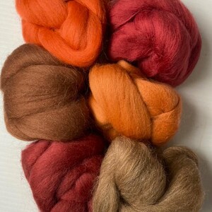 May include: Five balls of wool in shades of brown, orange, and red. The wool is arranged in a circle.