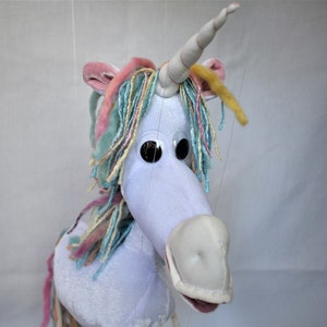 May include: A white unicorn puppet with a pink, blue, and yellow yarn mane and horn. The puppet has large black eyes and a white snout.