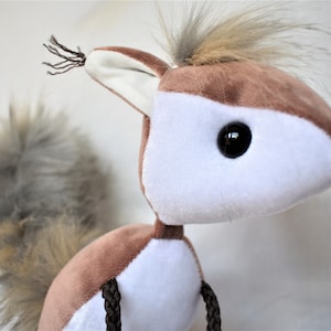 May include: A brown and white plush squirrel toy with a long, bushy tail. The squirrel has black eyes and a black nose.
