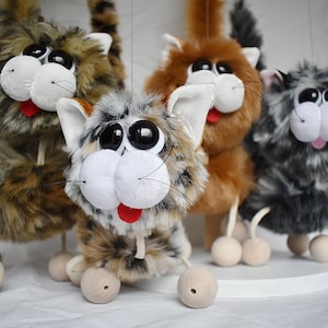 May include: Four plush cat puppets with large eyes and smiling mouths. Each puppet has a different fur pattern and color, including brown and black, gray and white, and brown and white. The puppets are on wooden wheels and have long tails.