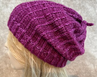 May include: A purple knitted beanie with a slouchy fit. The beanie is made with a textured stitch pattern.