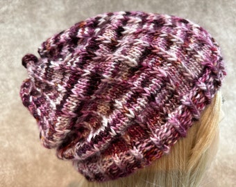 May include: A purple, pink, and white knitted beanie hat with a slouchy fit.