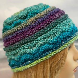May include: A knitted hat with a green, blue, and purple color scheme. The hat is made with a textured stitch and has a folded brim.