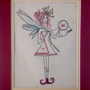 May include: Embroidered artwork of a fairy with a blue and white wing, holding a hoop with a red butterfly inside. The fairy is wearing a red and white dress with a yellow bow in her hair.