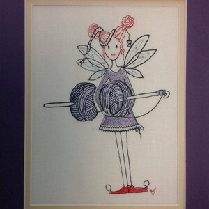 Könnte beinhalten: Gestickte Abbildung einer Fee mit rosa Haaren und Flügeln, die zwei Knäuel Wolle hält. Die Fee trägt ein lila Kleid und rote Schuhe.