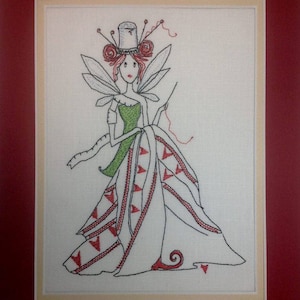 May include: Embroidered image of a fairy with red hair, wearing a green dress and a hat with red flowers. She is holding a needle and thread and is surrounded by red and white triangles.