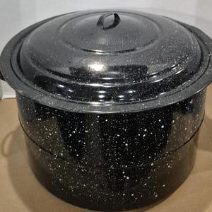 May include: A large, black speckled enamelware pot with a matching lid. The pot has a rounded shape with a wide rim and two handles. The lid has a loop handle. The pot is likely used for cooking or canning.